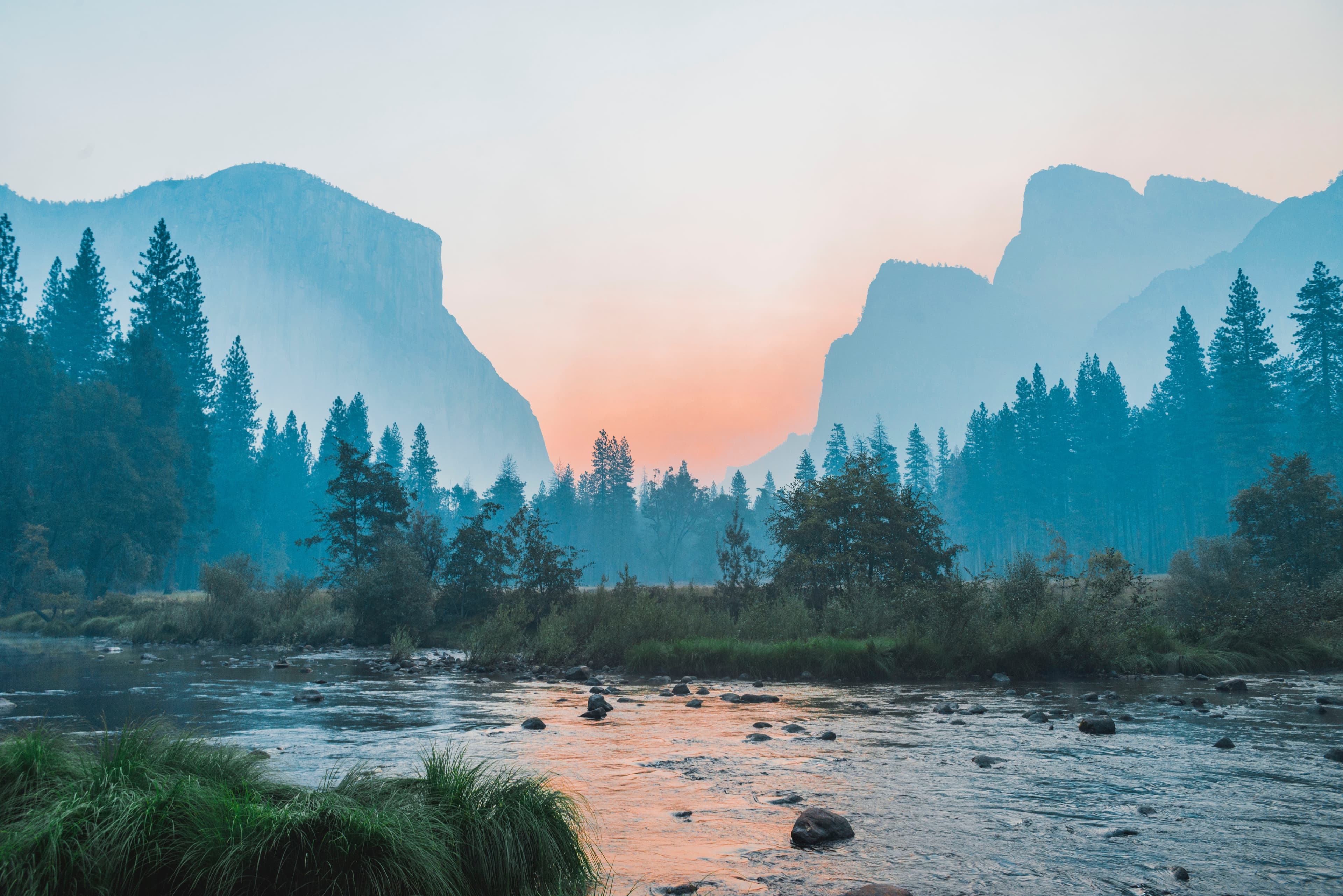 Shallow river at sunset with foliage and mountains in the background